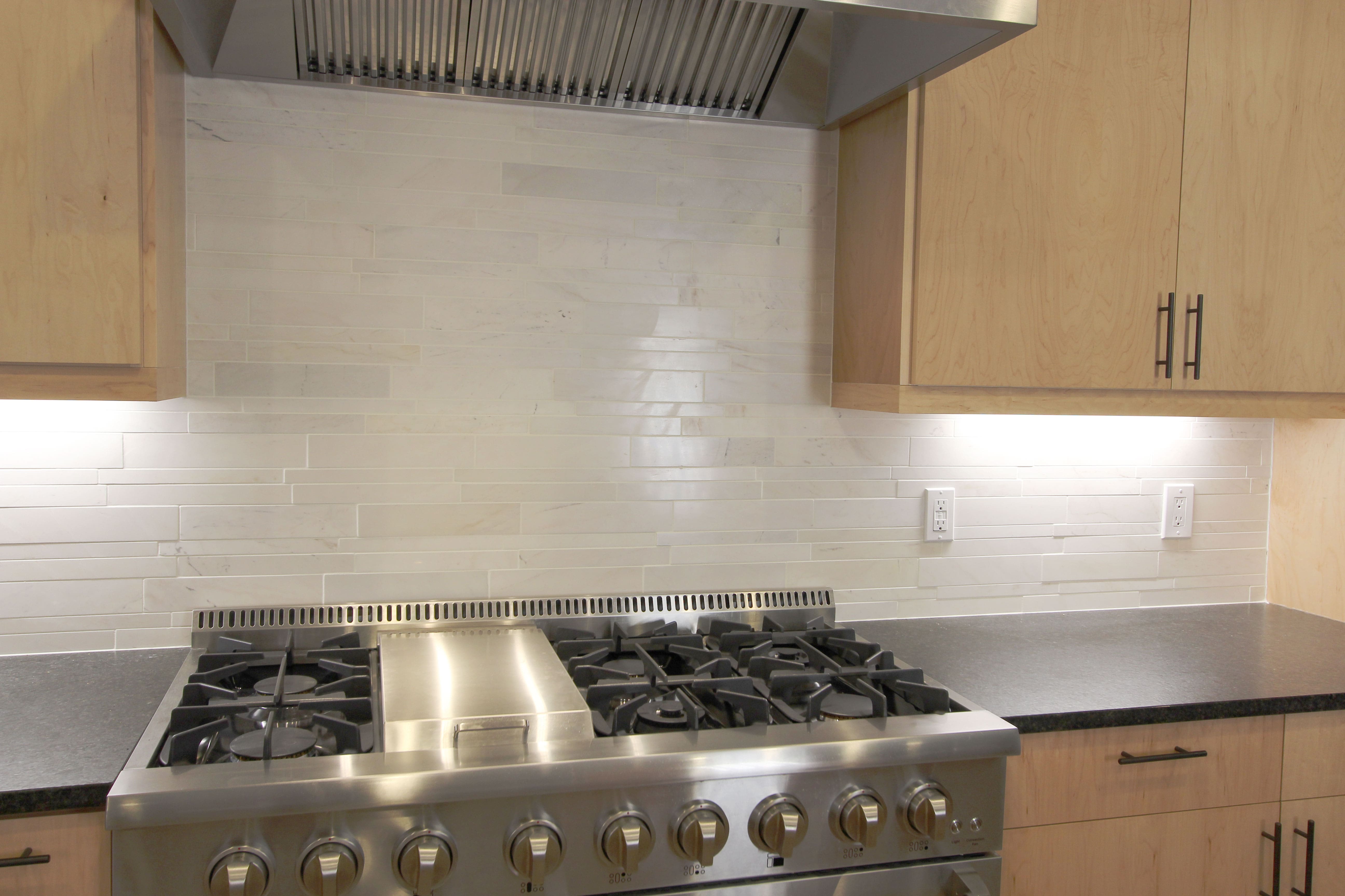 Norstone White Marble Lynia Interlocking Tiles used on a kitchen backsplash set against a large 6 burner stainless steel range and vent hood